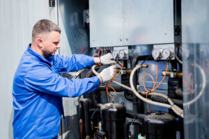 HVAC technician inspecting and servicing commercial heating and cooling system compressors and pressure gauges
